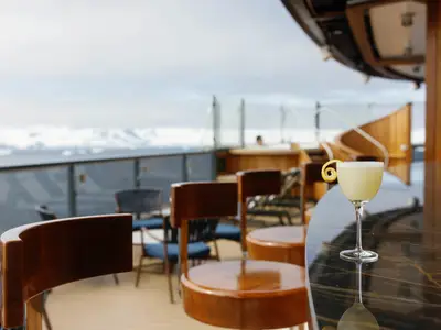Ein gelber Cocktail auf einer edlen Holz-Außenbar an Bord der Seabourn Venture vor einer eisigen arktischen Kulisse.