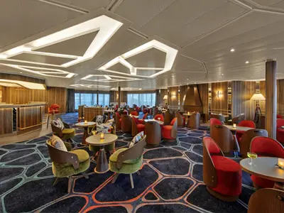 Die stilvolle Bar-Lounge an Bord der Seabourn Venture besticht durch geometrische Lichtelemente an der Decke und gemütliche grüne und rote Sessel.