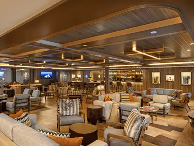 Blick in die elegante Lounge an Bord der Seabourn Venture mit bequemen Sesseln, warmem Licht und einer Bar im Hintergrund.