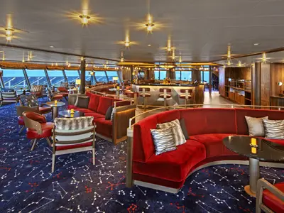 Die luxuriöse Constellation Lounge an Bord der Seabourn Venture mit geschwungenen roten Sofas, Sternen-Teppich und Bar.