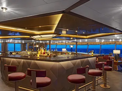 Elegante Bar mit polygonaler Theke, roten Barhockern und großen Fenstern mit Meerblick an Bord der Seabourn Venture.