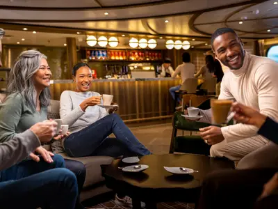 Eine Gruppe von gut gelaunten Passagieren genießt Kaffeespezialitäten in einer eleganten Lounge an Bord der Seabourn Venture.