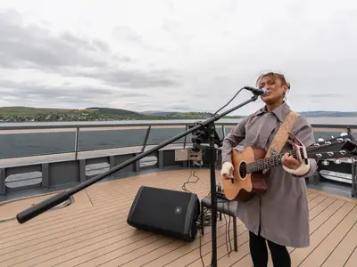 Eine Sängerin mit Akustikgitarre tritt bei einer Live-Performance auf dem Außendeck an Bord der Seabourn Venture auf.