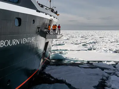 Die Seabourn Venture fährt durch dichtes Treibeis in der Arktis, während Passagiere von einer Aussichtsplattform aus zusehen.