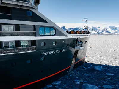 Die Seabourn Venture fährt durch dichtes Treibeis in polaren Gewässern vor einer eindrucksvollen Kulisse aus schneebedeckten Bergen.