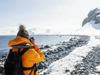 Eine Person in gelber Expeditionsjacke fotografiert die verschneite Küste der Antarktis während einer Reise mit der Seabourn Venture.