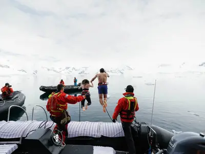 Zwei Gäste springen bei einem Polar Plunge von einem Zodiac-Schlauchboot der Seabourn Venture in das eisige Wasser der Antarktis.