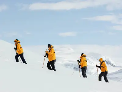 Vier Personen in gelben Parkas wandern bei einer Expedition der Seabourn Venture durch eine verschneite antarktische Berglandschaft.