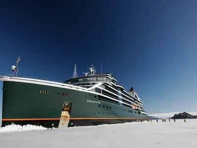 Die Seabourn Venture liegt im antarktischen Eis, während Passagiere davor auf dem Eis wandern.