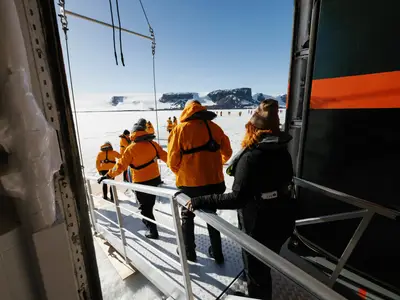 Passagiere in orangefarbenen Parkas steigen über eine Rampe der Seabourn Venture hinab auf das weite Eis der Antarktis.