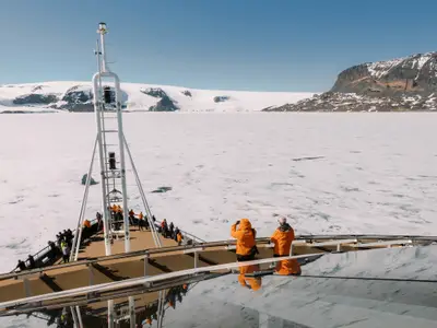 Passagiere in warmen Jacken stehen auf dem Außendeck der Seabourn Venture und blicken auf eisige Gewässer und ferne Berge.
