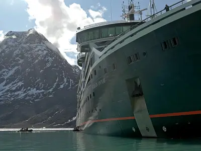 Außenansicht der Seabourn Venture in Grönland vor einem schneebedeckten Berg auf ruhigem Wasser mit Zodiac-Booten.
