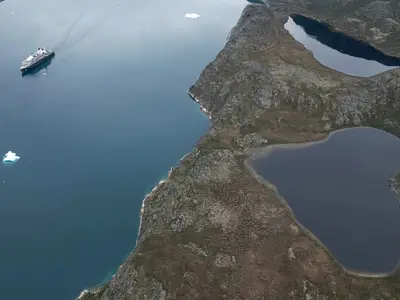 Eine spektakuläre Drohnenaufnahme der Seabourn Venture, die an der rauen Küste Grönlands mit einem herzförmigen See vorbeifährt.