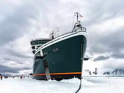 Die beeindruckende Bugansicht der Seabourn Venture, die im eisigen Meer der Antarktis liegt, während Gäste auf dem Packeis spazieren.