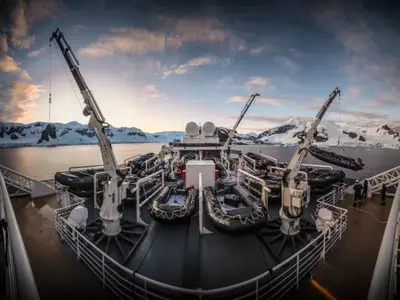 Blick über das Außendeck der Seabourn Venture mit zahlreichen Zodiac-Schlauchbooten und Kränen vor einer eisigen Bergkulisse in der Antarktis.