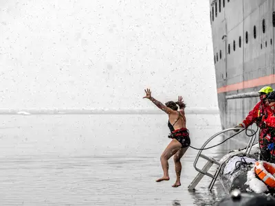 Eine Frau im Badeanzug springt bei Schneefall von der Seabourn Venture ins eiskalte Meerwasser, gesichert von der Crew.