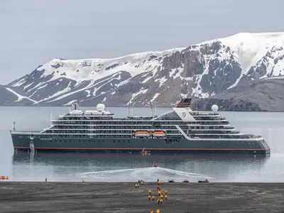 Das Expeditionsschiff Seabourn Venture ankert in einer Bucht der Antarktis mit schneebedeckten Bergen im Hintergrund und Kajakern am Strand.
