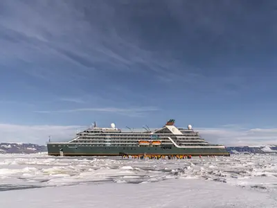 Das Expeditionsschiff Seabourn Venture umgeben von Eis und Gletschern in der Antarktis, mit einer Gruppe von Passagieren davor auf dem Eis.