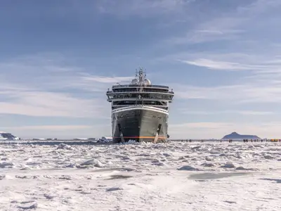 Frontalansicht des Expeditionsschiffs Seabourn Venture im dicken Packeis der Antarktis mit Passagieren auf der Eisflaeche.