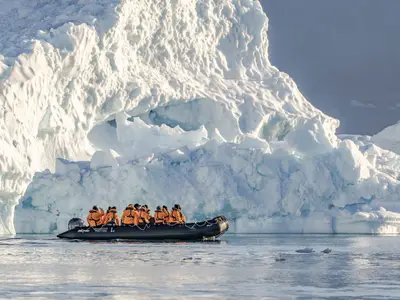 Passagiere in orangefarbenen Jacken fahren in einem Schlauchboot der Seabourn Venture dicht an einer gewaltigen Eiswand vorbei.