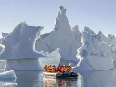 Ein Zodiac-Schlauchboot mit Passagieren der Seabourn Venture fährt vor gigantischen, bizarr geformten Eisbergen im arktischen Gewässer.