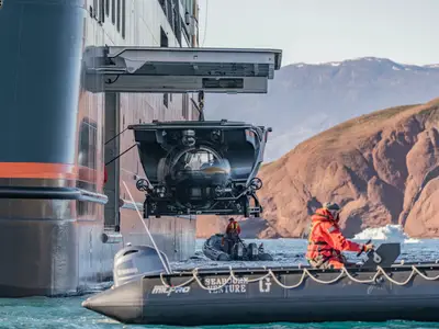 Ein U-Boot wird an der Seite der Seabourn Venture herabgelassen, umgeben von Schlauchbooten vor einer arktischen Bergkulisse.