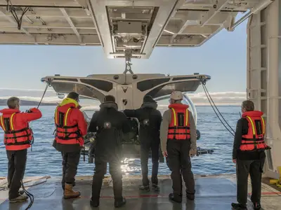 Crewmitglieder in Sicherheitswesten stehen an Bord der Seabourn Venture vor einem U-Boot auf dem Außendeck über dem Meer.
