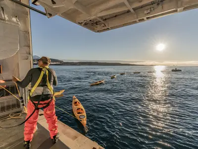 Ein Guide an Bord der Seabourn Venture sichert gelbe Kajaks an der Heckplattform für einen Ausflug auf dem ruhigen Meer.