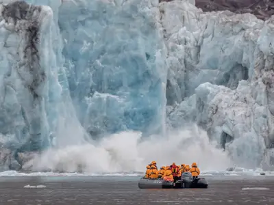 Gäste der Seabourn Venture in einem Schlauchboot beobachten das Kalben eines riesigen blauen Gletschers in der Arktis.