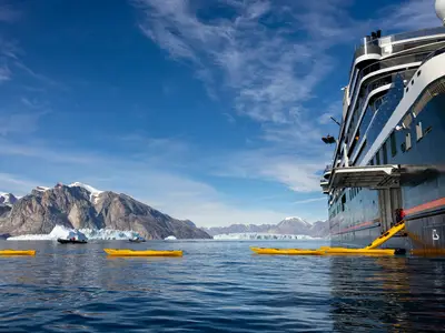 Gelbe Kajaks werden über eine Rampe der Seabourn Venture in ein arktisches Gewässer vor eisiger Bergkulisse gelassen.