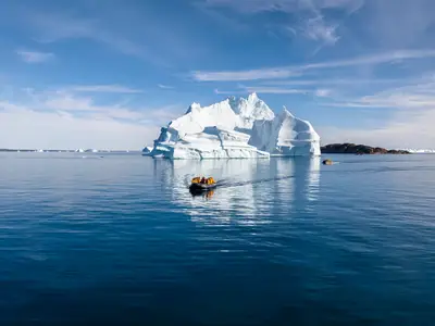 Gäste der Seabourn Venture fahren in Zodiac-Booten auf dem ruhigen Meer nahe eines gigantischen Eisbergs.