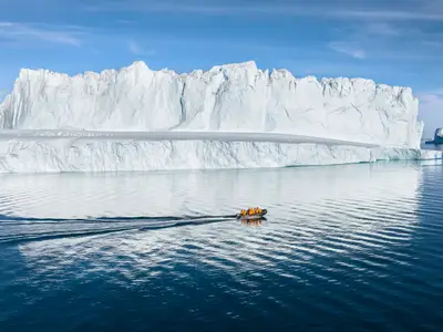 Ein Zodiac-Schlauchboot der Seabourn Venture fährt bei einer Arktis-Expedition an einer riesigen Eisberg-Wand vorbei.