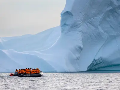 Passagiere der Seabourn Venture fahren in einem Zodiac-Schlauchboot an einer gigantischen Eisbergwand in der Arktis vorbei.