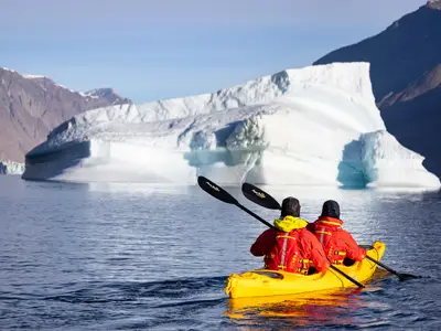 Zwei Kajakfahrer während eines Ausflugs der Seabourn Venture paddeln auf dem ruhigen Wasser vor einem riesigen Eisberg.
