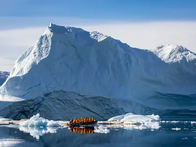 Passagiere der Seabourn Venture fahren in einem Zodiac-Schlauchboot ganz nah an einem riesigen Eisberg in der Arktis vorbei.