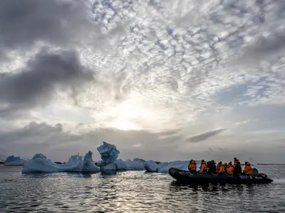 Passagiere der Seabourn Venture in einem Zodiac-Schlauchboot beobachten gigantische Eisberge in der eisigen Antarktis unter einem Wolkenhimmel.