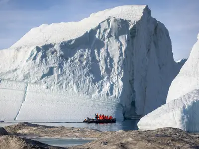 Ein Expeditionsschlauchboot der Seabourn Venture mit Gästen fährt im arktischen Gewässer nah an einer gigantischen Eisbergwand entlang.