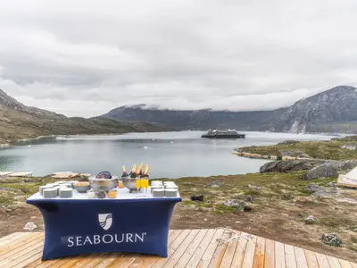 Ein elegant gedeckter Tisch mit Champagner und Kaviar vor der Kulisse Grönlands und der Seabourn Venture im Hintergrund.