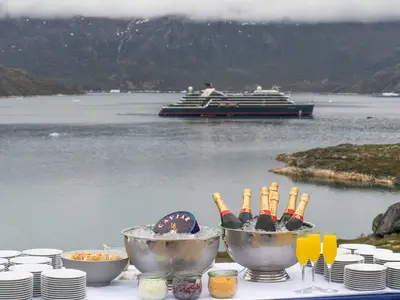 Ein Tisch mit Champagner und Kaviar auf Eis, im Hintergrund fährt die Seabourn Venture durch ein grönländisches Fjord.