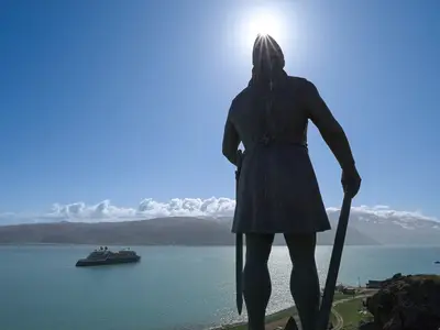 Eine Wikinger-Statue steht im Gegenlicht auf einem Hügel in Grönland, im Hintergrund liegt die Seabourn Venture im Wasser.