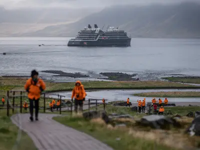 Gäste in orangefarbenen Jacken kehren von einem Landausflug zur im Fjord ankernden Seabourn Venture zurück.