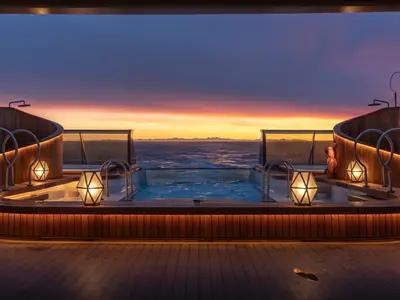 Ein symmetrischer Blick auf den Pool- und Whirlpoolbereich an Bord der Seabourn Venture bei einem spektakulären Sonnenuntergang auf dem Meer.
