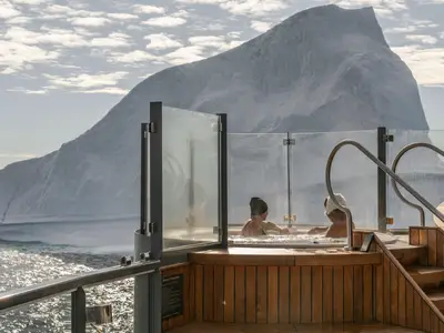 Zwei Personen entspannen im warmen Whirlpool an Bord der Seabourn Venture vor einer spektakulären Eisberg-Kulisse.