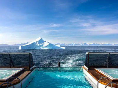 Der Infinity-Pool und zwei Whirlpools auf dem Außendeck der Seabourn Venture mit Blick auf einen riesigen Eisberg in der Arktis.