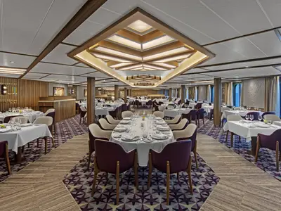 Das stilvoll eingerichtete Restaurant an Bord der Seabourn Venture mit gedeckten Tischen, lila Sesseln und einer kunstvollen Deckenbeleuchtung.