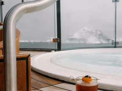 Ein dampfender Whirlpool auf dem Außendeck an Bord der Seabourn Venture mit Blick auf eisige Berge in polarer Landschaft.