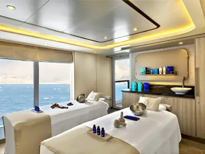 Zwei Massageliegen im Spa-Bereich an Bord der Seabourn Venture mit Blick durch das Fenster auf das Meer und Eisberge.