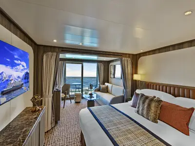 Blick in eine elegante Suite an Bord der Seabourn Venture mit großem Bett, gemütlichem Wohnbereich und Balkon mit Meerblick.