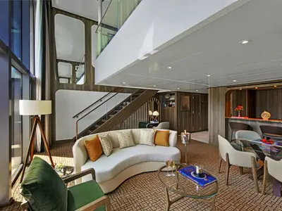 Blick in eine großzügige, zweistöckige Loft-Suite an Bord der Seabourn Venture mit geschwungenem Sofa, Essbereich, Bar und Holztreppe.