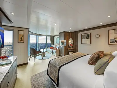 Luxuriöse Suite an Bord der Seabourn Venture mit großem Bett, Sitzecke und Panoramafenstern mit Blick auf eisige Gewässer.